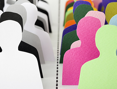 Zwei Reihen von Pappfiguren nebeneinander, wobei die linke schwarz-weiß und die rechts bunt ist.