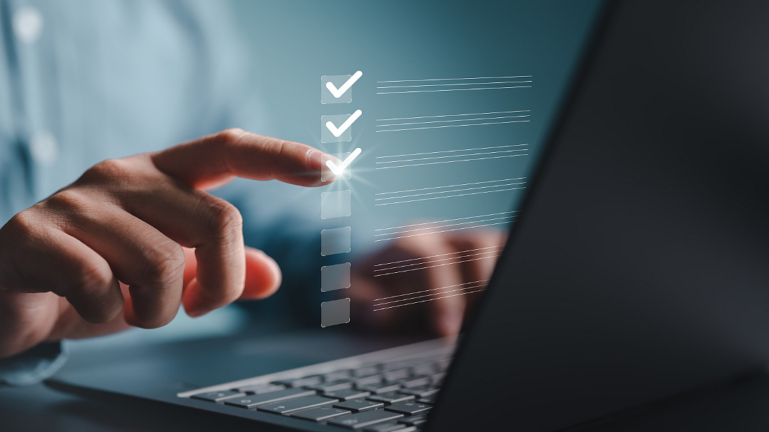 Hand markiert Kontrollkästchen auf einem schwebenden digitalen Formular vor einem Laptop