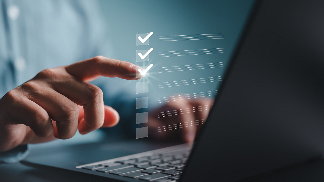 Hand markiert Kontrollkästchen auf einem schwebenden digitalen Formular vor einem Laptop