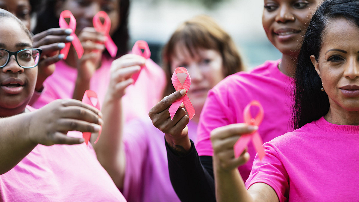 Gruppe von Frauen in pinken T-Shirts, die rosa Schleifen, als Symbole für Brustkrebs halten.