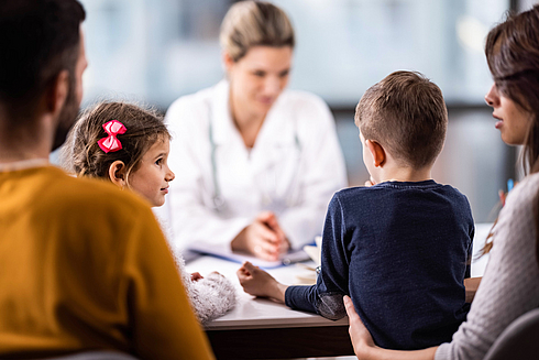 Familie mit zwei Kindern sitzt einer Ärztin am Tisch gegenüber in einem Beratungsgespräch.