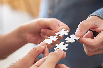 Mehrere Hände setzen gemeinsam ein weißes Puzzlestück zusammen.