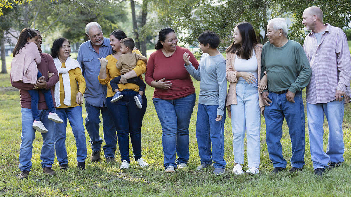 Große Mehrgenerationenfamilie unterhält sich im Freien unter Bäumen.